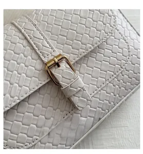 Close-up of white woven leather texture with a gold pin buckle closure on the baguette bag