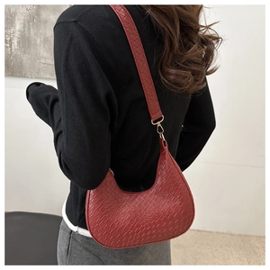 Detalle del bolso media luna rojo con textura de cocodrilo y correa ancha en modelo