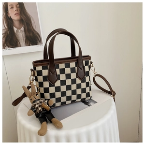 Detail of checkered canvas bag with brown leather handle and cute rabbit charm