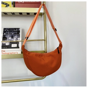 Minimalist orange nylon dumpling bag hanging on a gold rack with adjustable strap