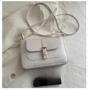 Detailed close-up of white woven leather baguette bag with gold metal buckle and phone for scale