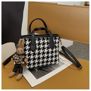 Detail of houndstooth crossbody bag with a cute rabbit pendant on a leather chair