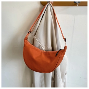 Detailed view of an orange nylon crescent crossbody bag hanging against a beige blazer