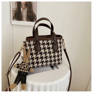 Detail of houndstooth fabric bag with brown leather handles and a cute rabbit charm accessory