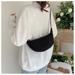 Rear view of a model wearing a black nylon crescent crossbody bag in a minimalist setting