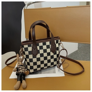 Detail view of checkerboard pattern bag with a cute rabbit plush pendant on a chair