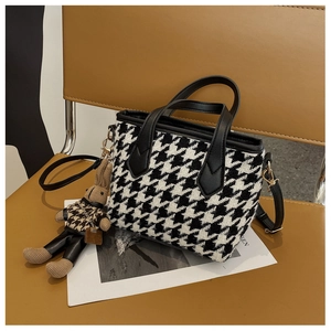 Detail of houndstooth tote bag with leather handles and cute bunny charm on leather chair