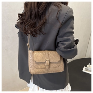 Close-up of woven crocodile texture on beige shoulder bag against grey suit fabric