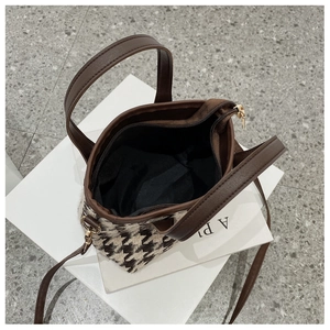 Detail view of houndstooth crossbody bag with brown leather trim and zipper closure