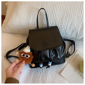 Detail of black faux leather mini backpack with flap closure and cute plush bear charm