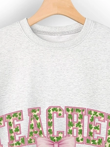 Detail of the TEACHER print with clover pattern and a pink bow on a gray sweatshirt