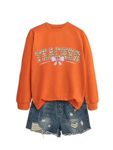 Detail of orange crewneck teacher sweatshirt with floral lettering and denim shorts