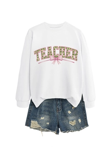 Flat lay of a white sweatshirt with clover pattern TEACHER text and denim shorts