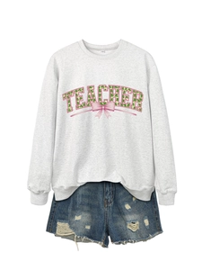 Close-up of TEACHER sweatshirt with clover patterns and a pink bow on gray fabric