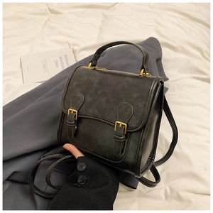 Top-down view of a vintage black matte crossbody bag on grey blazer and white cloth
