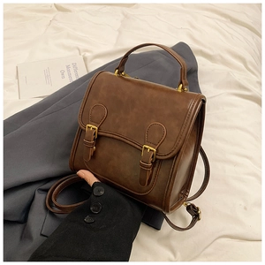 Detail of a vintage dark brown satchel bag with gold buckles on a grey blazer background