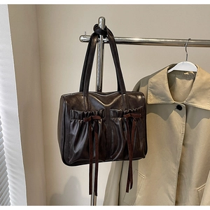 Detail of dark brown tote bag with ruffled pockets and decorative ribbon bows