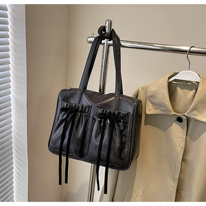 Detail of black leather tote bag with pleated pockets and ribbon bow on beige coat