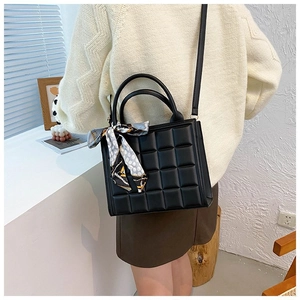 Quilted black crossbody bag with decorative silk scarf shown on a model