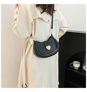 Détail du sac de selle noir avec fermoir cœur doré porté sur un trench-coat beige