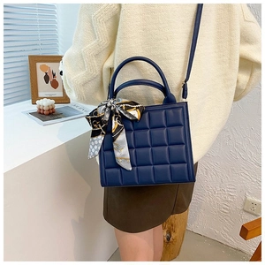 Detail of navy blue quilted tote bag featuring a decorative silk scarf on the handle
