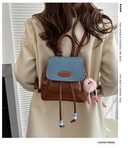 Detail of blue denim and brown leather backpack with pink fur charm on model