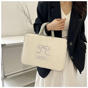 Close-up of cream laptop bag with purple bow embroidery and green handles in hand
