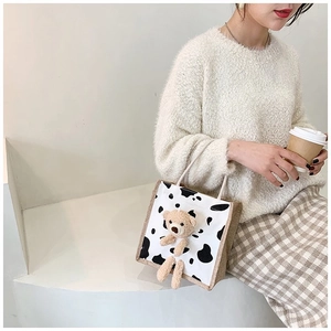 Detail of canvas tote bag featuring cow print and a 3D plush bear on minimalist background