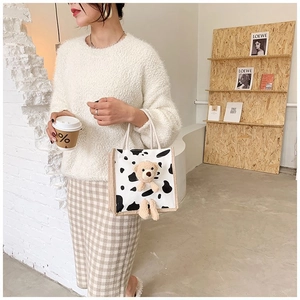 Detail of cow-print canvas tote bag featuring a cute 3D plush teddy bear and rope handles