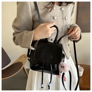 Detail of black leather bag with embossed logo and pink plush monster charm on tweed jacket