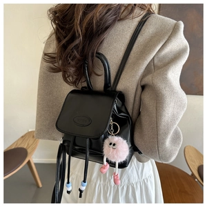 Detail of a black PU leather mini backpack with beaded drawstrings and a pink plush charm