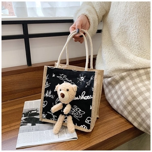 Detail of canvas handbag featuring white graffiti print and brown plush bear charm