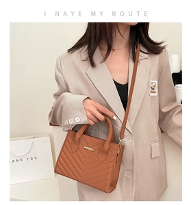 Close-up of brown crossbody bag with V-shaped stitching and metallic JINGPIN logo detail
