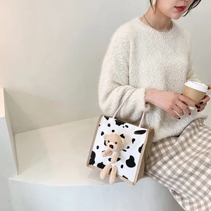 Cute cow print mini handbag with a 3D plush bear detail and light brown canvas handles