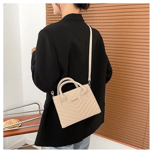 Detailed view of beige quilted crossbody bag styled with a professional black blazer