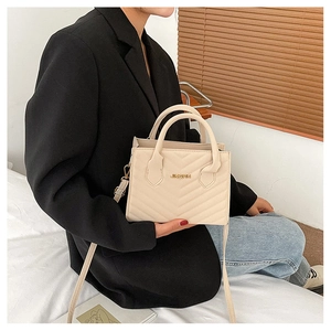 Close-up of beige V-quilted crossbody bag with gold logo and detachable strap on model