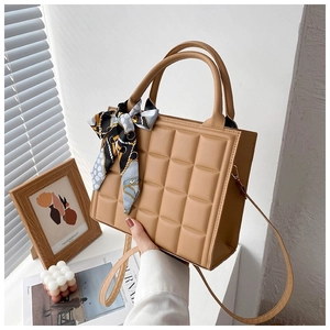 Detail of khaki square tote bag with grid embossing and decorative silk scarf handle