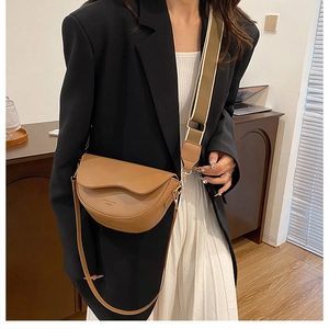 Detail of a brown leather saddle bag featuring a wide fabric strap and gold hardware