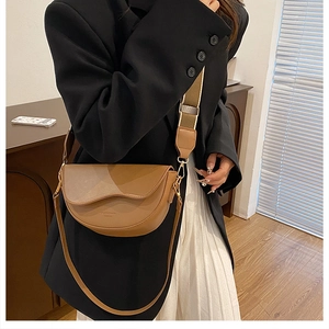Brown saddle bag featuring a wave-edge flap and wide fabric shoulder strap with gold hooks
