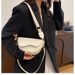 Detail of off-white crescent saddle bag with wide strap and gold hardware on model
