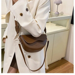 Close-up of brown saddle bag with wave-edged flap and fabric strap on white trench coat