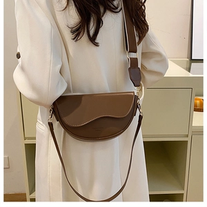 Detailed side view of brown saddle bag with wavy flap edge and wide shoulder strap