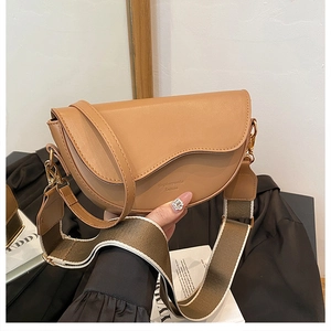 Detailed close-up of camel saddle bag featuring asymmetric flap and woven guitar strap