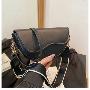 Close-up of black leather saddle bag with gold hardware and stylish woven shoulder strap