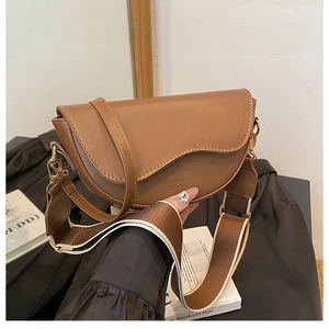 Detail of brown saddle bag with wavy flap design and wide fabric shoulder strap