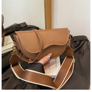 Close-up of brown leather saddle bag featuring dual straps and wide canvas shoulder strap