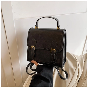 Detail of vintage black matte leather backpack with gold buckles and top handle grip