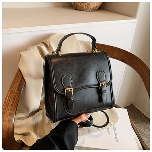 Detailed view of a vintage black leather bag with gold buckles on a wooden chair