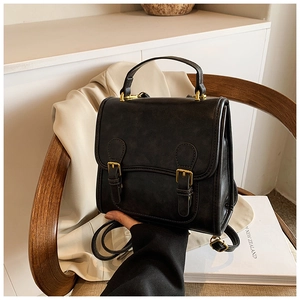 Detail of vintage black matte leather backpack with gold buckles on a wooden seat