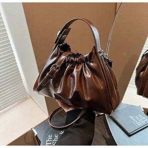 Détail d'un sac à main marron foncé brillant avec plis, ferrures et deux bandoulières